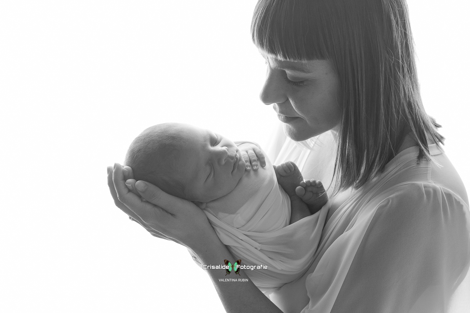 Scatto in bianco e nero realizzato durante un corso di mentoring fotografico sulla fotografia newborn base, nello studio di Elisa Spreafichi a Pianiga, in provincia di Venezia. Una mamma tiene dolcemente tra le mani il neonato fasciato, in un momento di intensa tenerezza