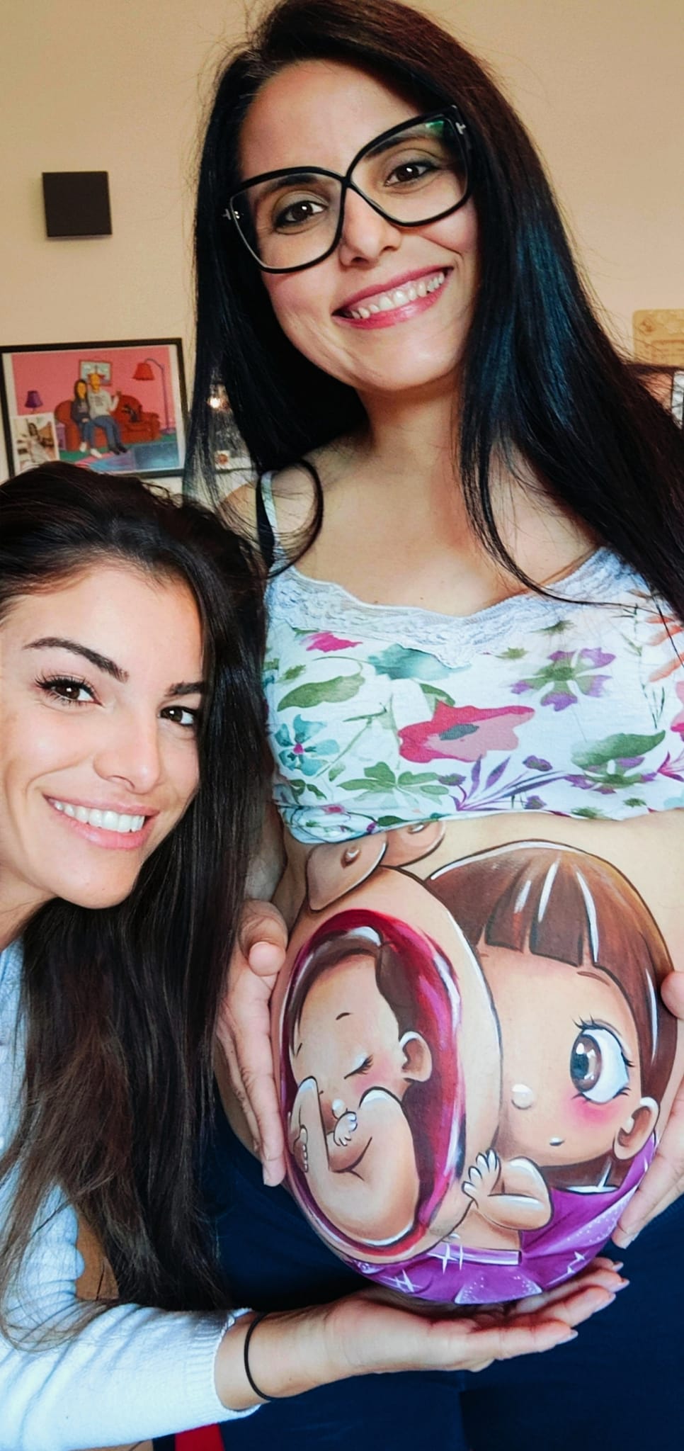 L'artista Jenny Corrò JeJe in un selfie sorridente insieme a una mamma in gravidanza a Borgoricco, Padova, mostrando il belly painting sul pancione con i disegni del bebè e della sorellina