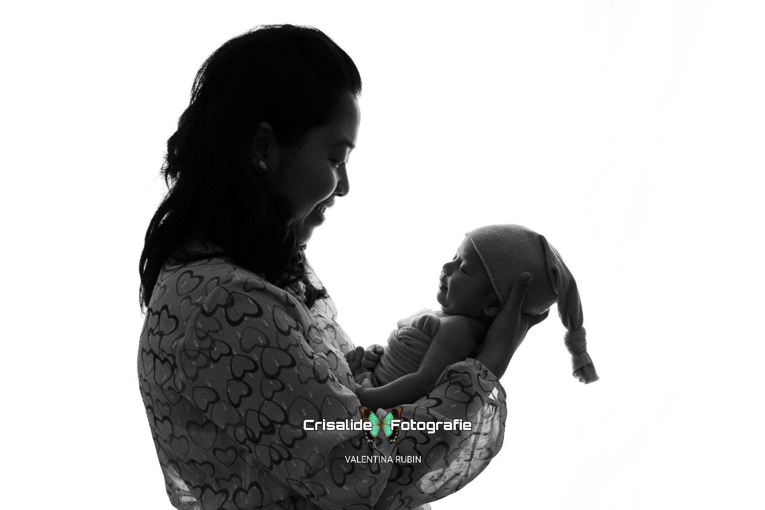 Mamma tiene in braccio il neonato avvolto in fascia beige, uno di fronte all'altro, scatto newborn in bianco e nero su sfondo bianco