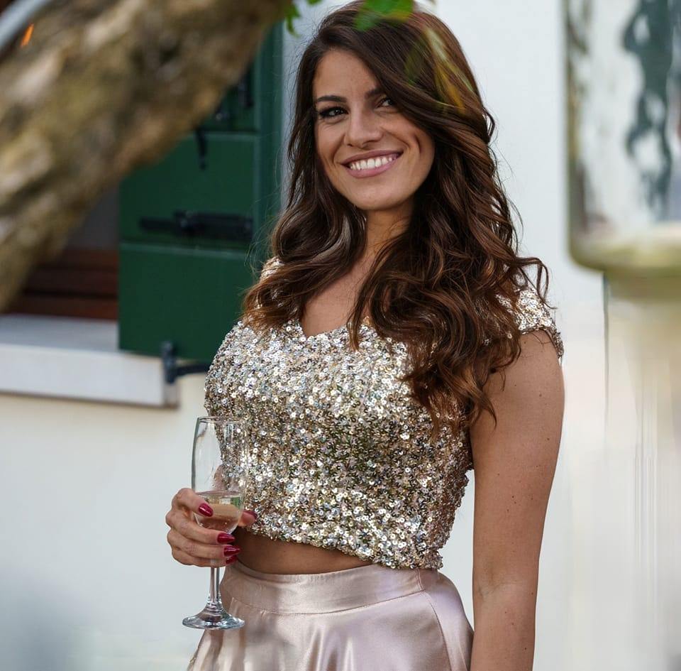 Jenny Corrò nel giorno del suo 40° compleanno, sorridente con corpetto in pailettes oro, mentre tiene in mano un bicchiere di vino bianco, e capelli sulle spalle mori e ondulati