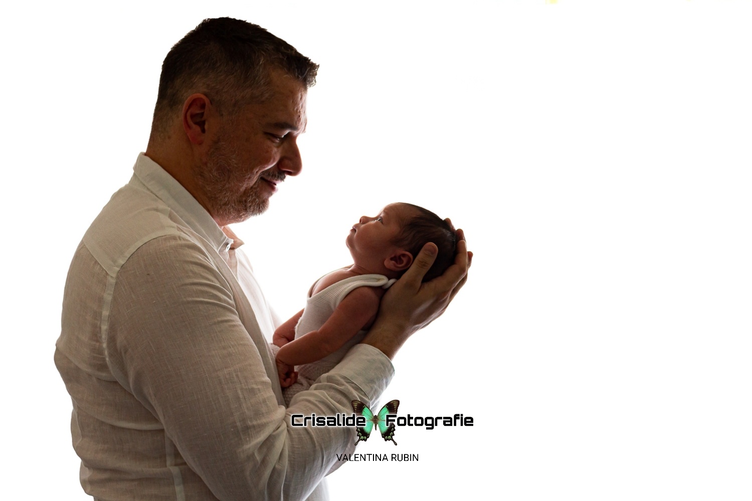 Papà sorride guardando il neonato vestito con body bianco, testina sorretta dalle mani del papà, sfondo bianco