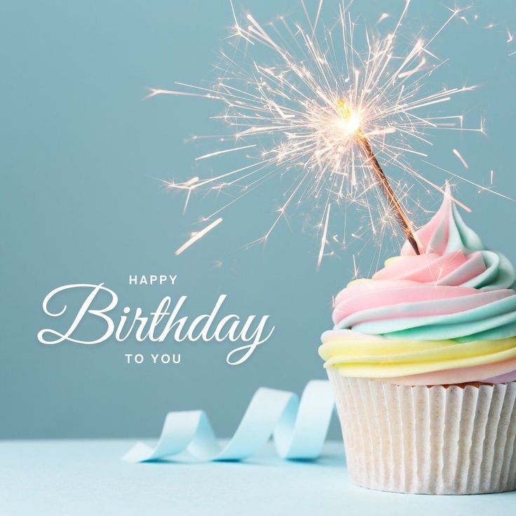 Cupcake in primo piano, con una candelina che fa scintille, sfondo azzurro e scritta bianca Happy birthday to you