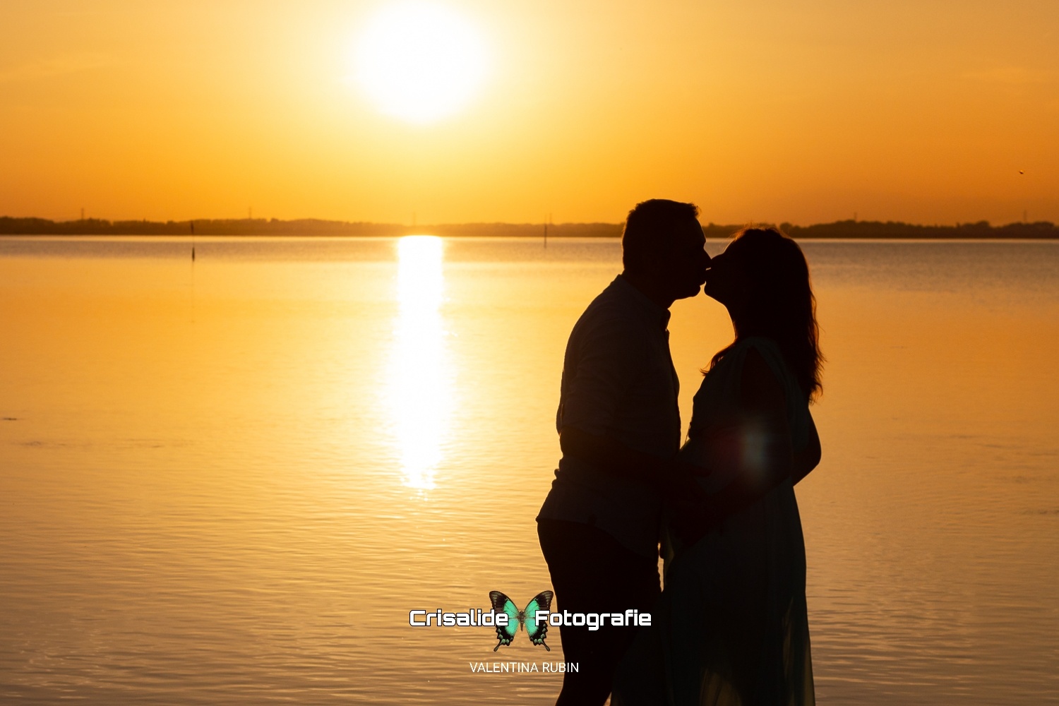 Silhouette di una coppia che si bacia in controluce, sullo sfondo il mare illuminato dal sole al tramonto, colori arancioni e silhouette nere