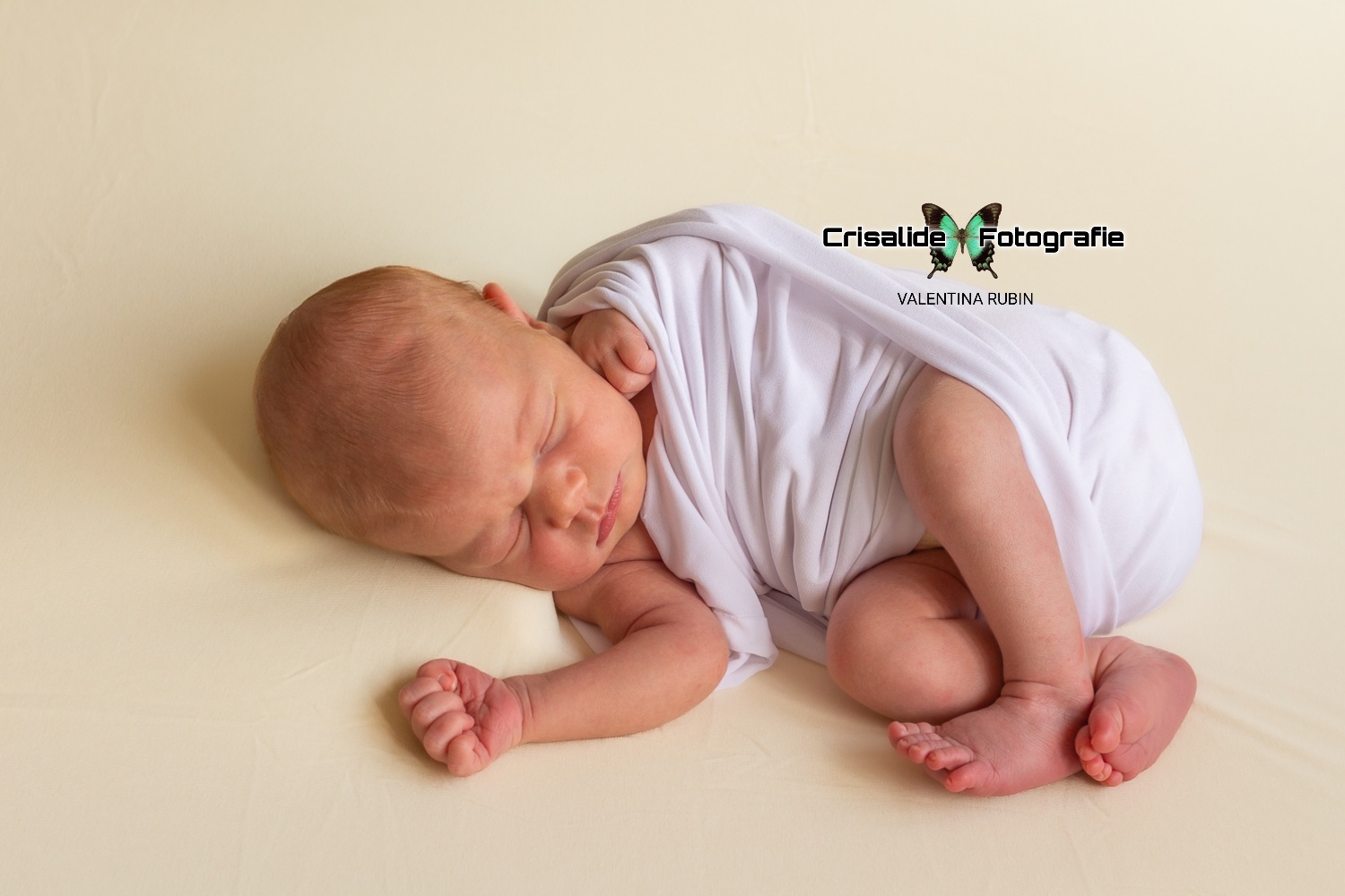 Neonata che dorme. girata su un fianco, fasciata di bianco, sfondo beige