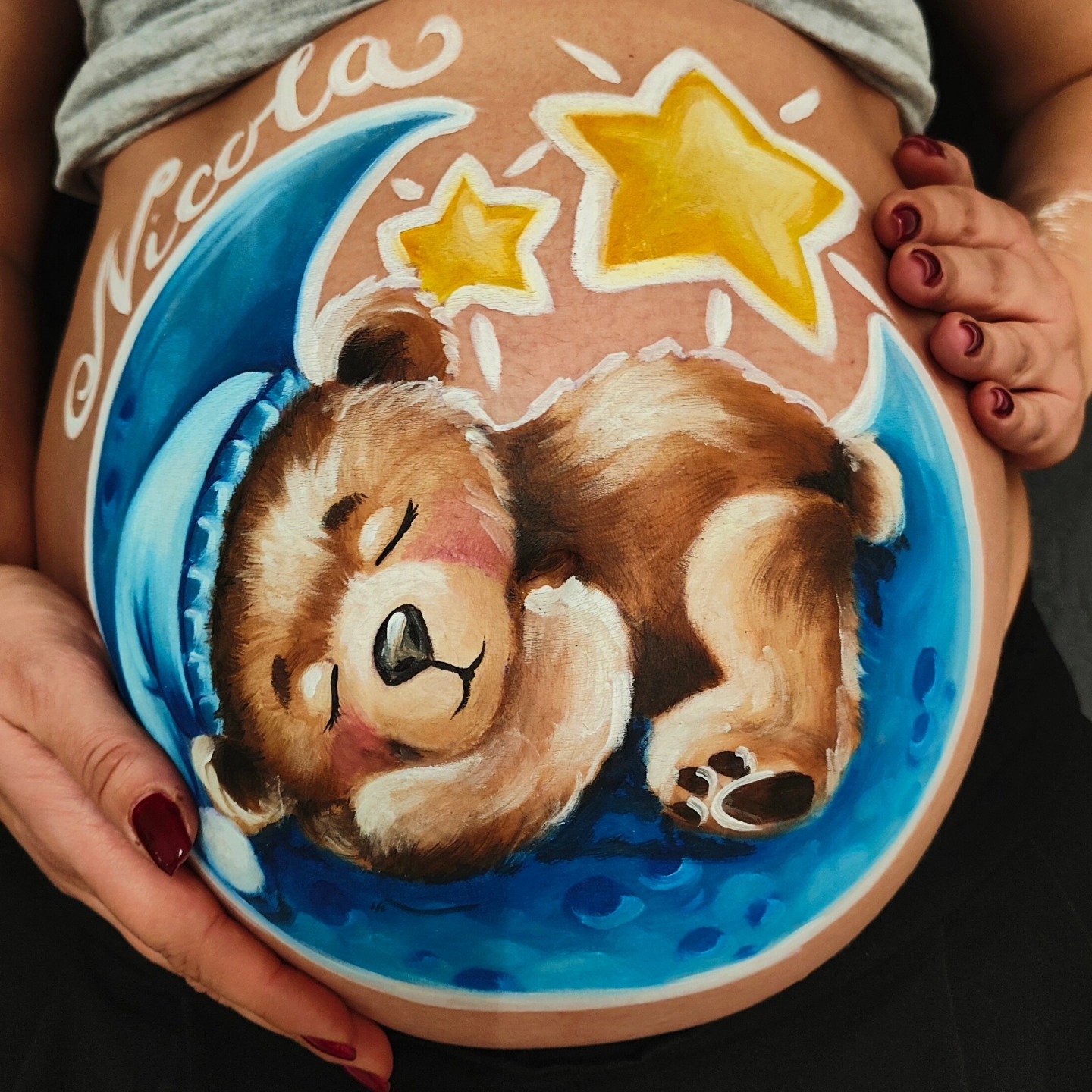 Belly painting sul pancione con un orsacchiotto che dorme sulla luna, stelline e la scritta Nicola, opera di Jenny Corrò JeJe