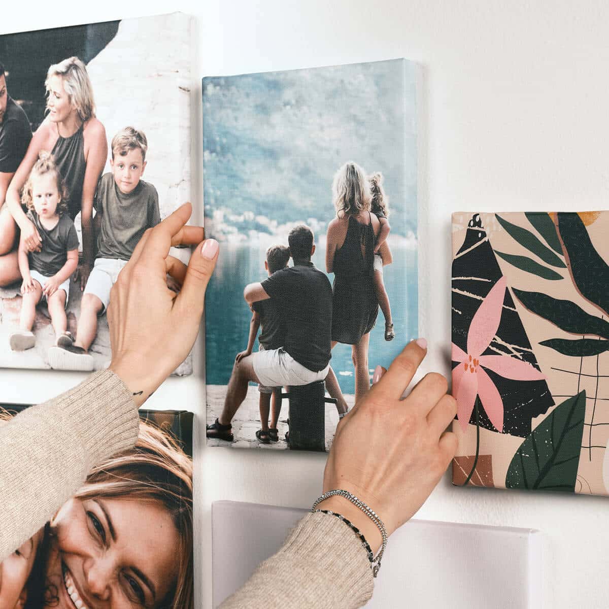 Quattro stampe su tela appese al muro, con due mani che sistemano la stampa centrale. Composizione ordinata e luminosa che mostra il risultato finale delle stampe su tela