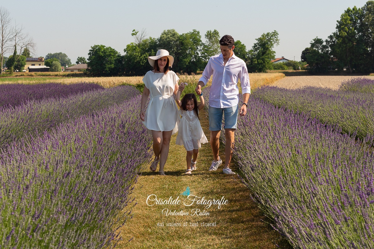 Famiglia che cammina nel campo di lavanda, mamma, papà e figlia che si tengono per mano sorridendo