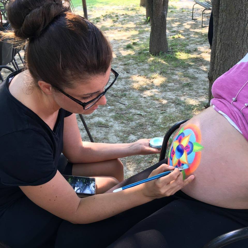 L'artista Jenny Corrò JeJe mentre realizza un disegno di belly painting colorato sul pancione di una mamma in gravidanza