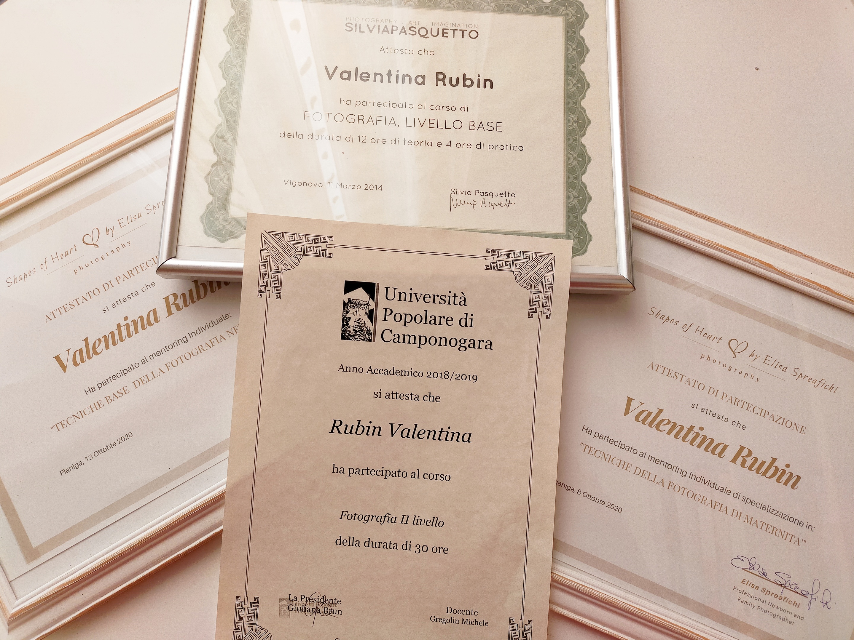 Quattro attestati di corsi di fotografia di Valentina Rubin, disposti su sfondo bianco: tre orizzontali a formare una Y rovesciata e uno verticale al centro in basso, a testimonianza del percorso di formazione continua in fotografia di maternità e neonati e crescita personale