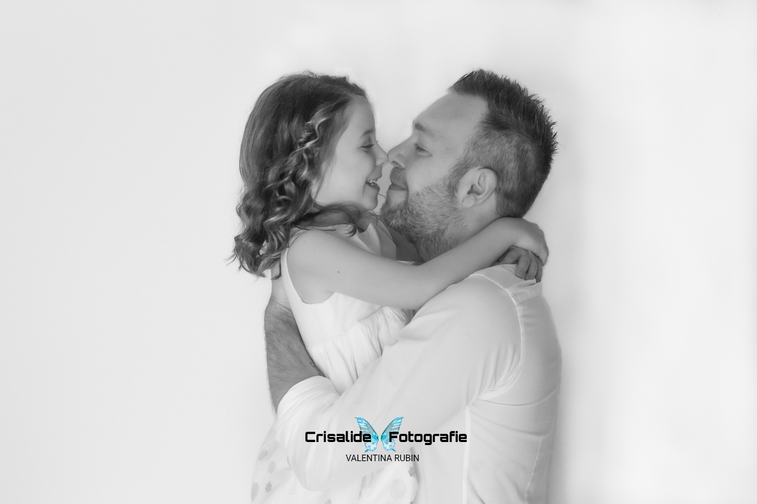 Ritratto in bianco e nero di un papà che tiene in braccio la figlia: si toccano i nasi e sorridono, momento spontaneo e affettuoso