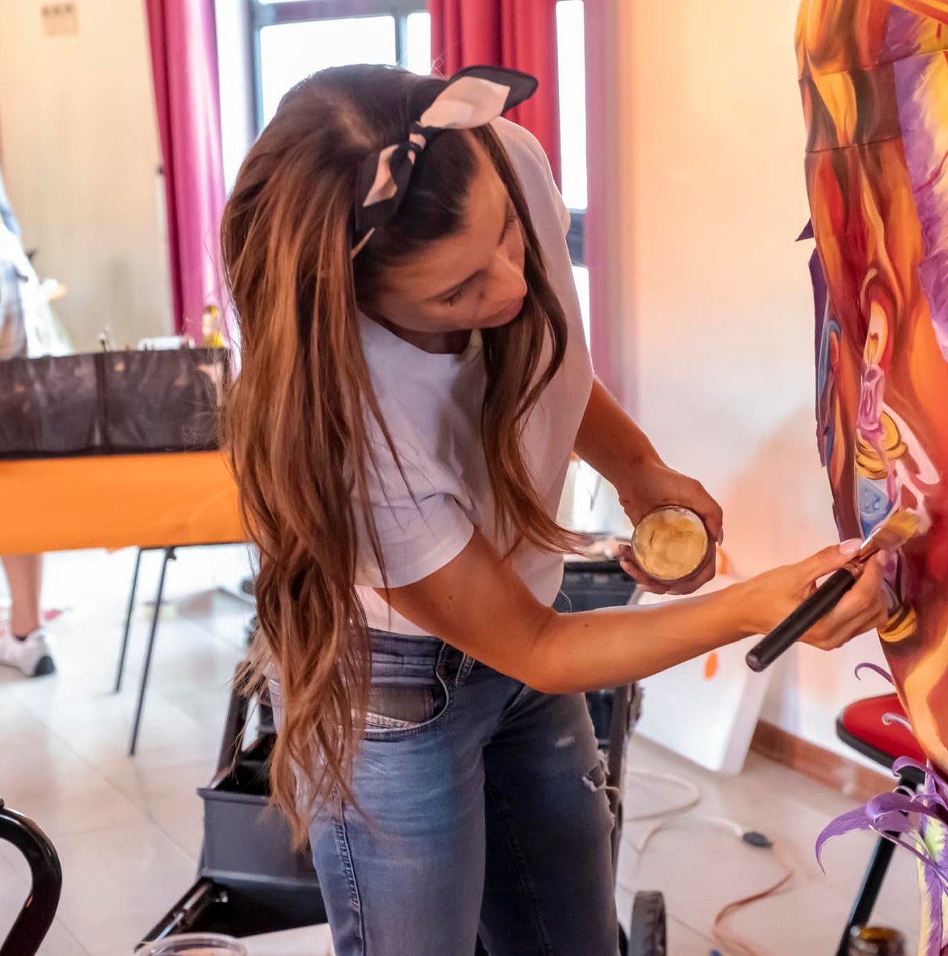 Jenny Corrò con jeans, maglietta bianca, fiocco in testa mentre dipinge un quadro