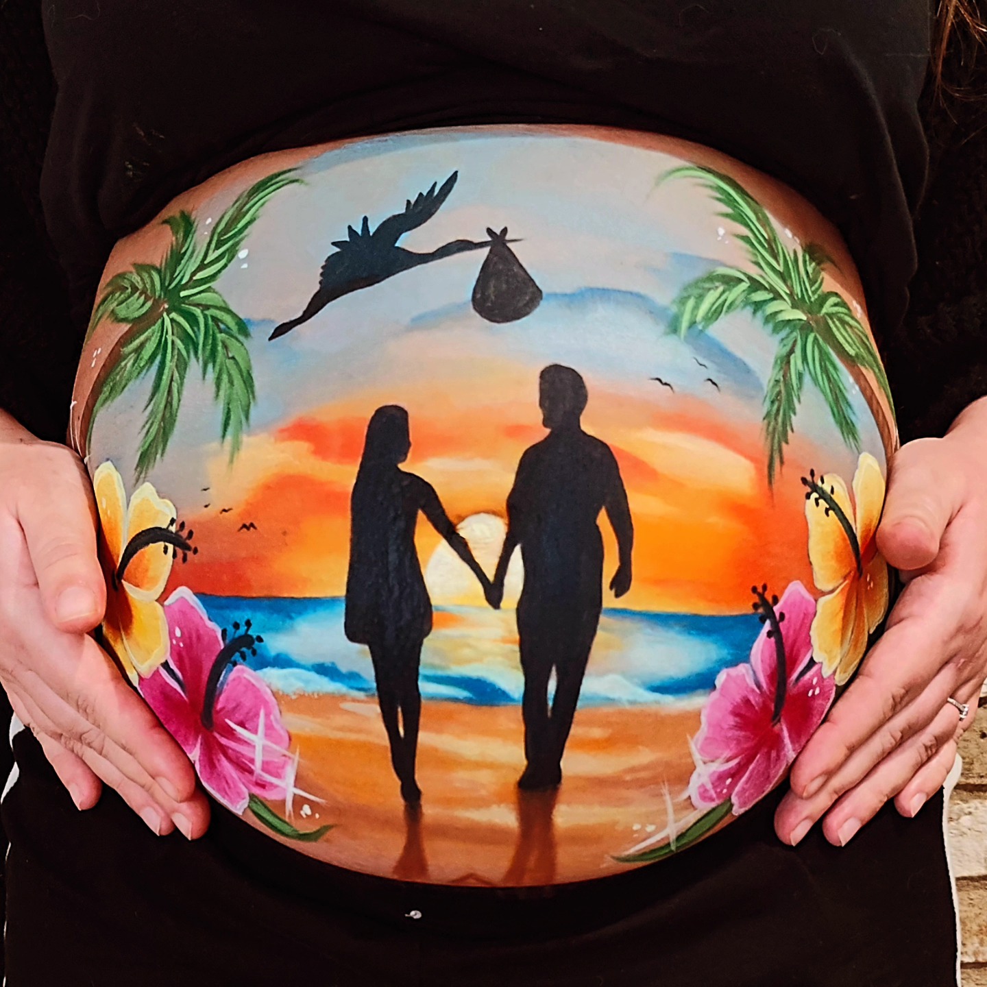 Primo piano del pancione di una mamma con belly painting disegno 2 silhouette di una coppia con silhouette di una cicogna con sacco al tramonto