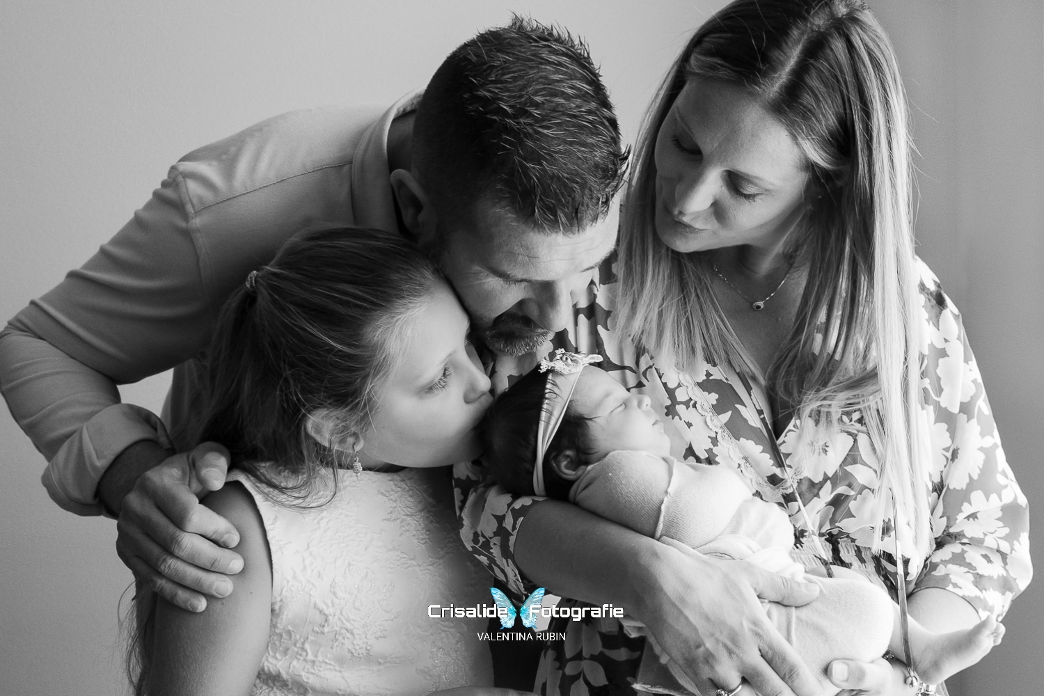 Mamma, papà e bambina insieme alla neonata che dorme, baci sulla testina, scatto newborn in bianco e nero