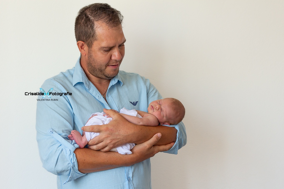 Papà in camicia azzurra che guarda la neonata addormentata tra le sue braccia, su sfondo bianco