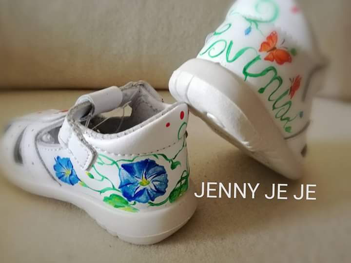 Scarpette bianche da bambina dipinte a mano con fiori blu, farfalle e il nome Lavinia, opera personalizzata di Jenny Corrò JeJe