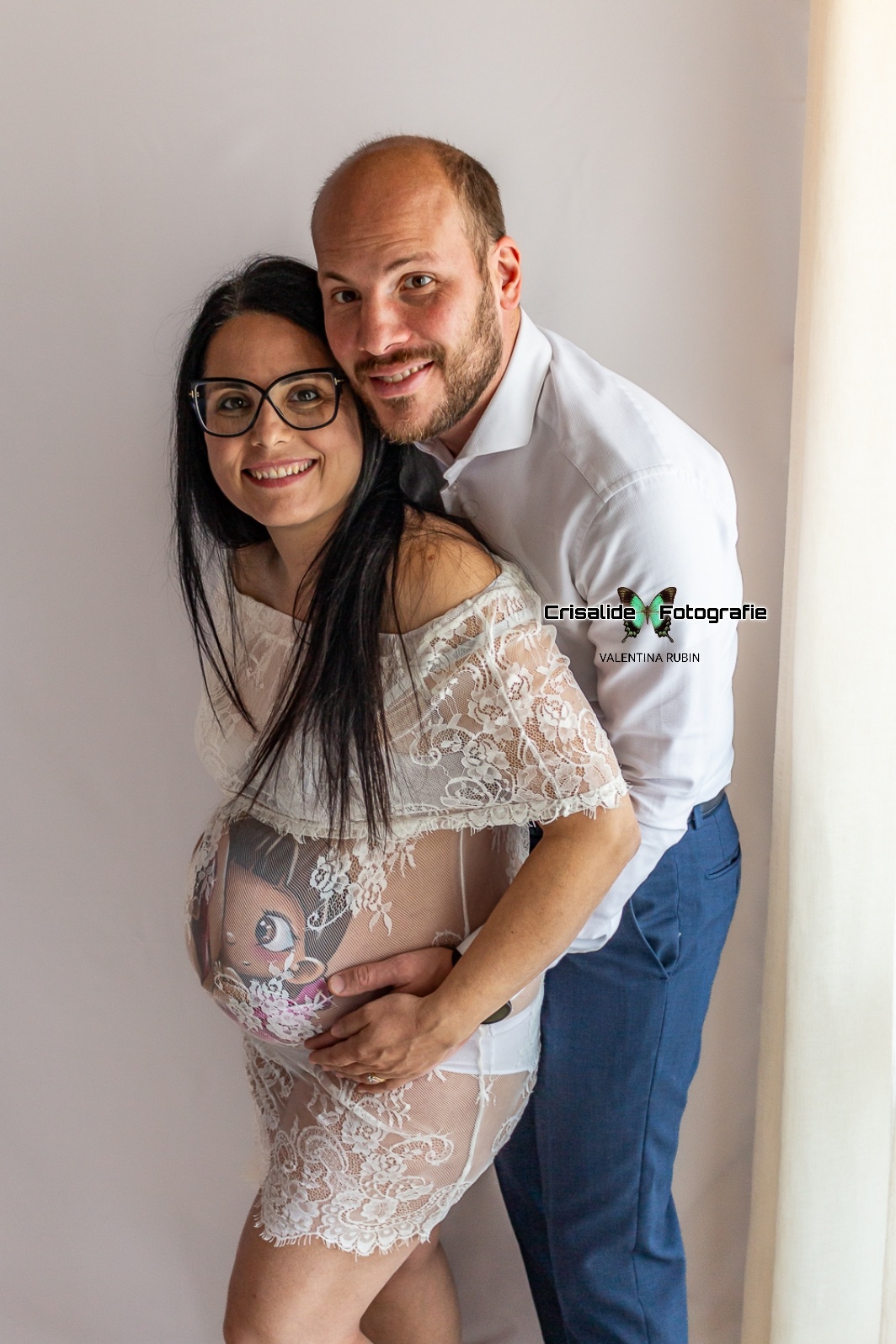 Mamma incinta con papà dietro che l'abbraccia, entrambi mani sul pancione con belly painting