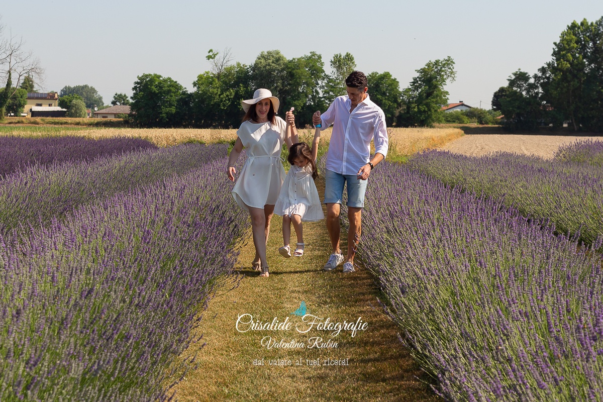 Mamma, papà e bambina vestiti di bianco nel campo di lavanda, papà e mamma sollevano la bambina in un piccolo salto, servizio fotografico famiglia all'aperto, momenti autentici di gioia, abbracci e sorrisi sotto il cielo azzurro