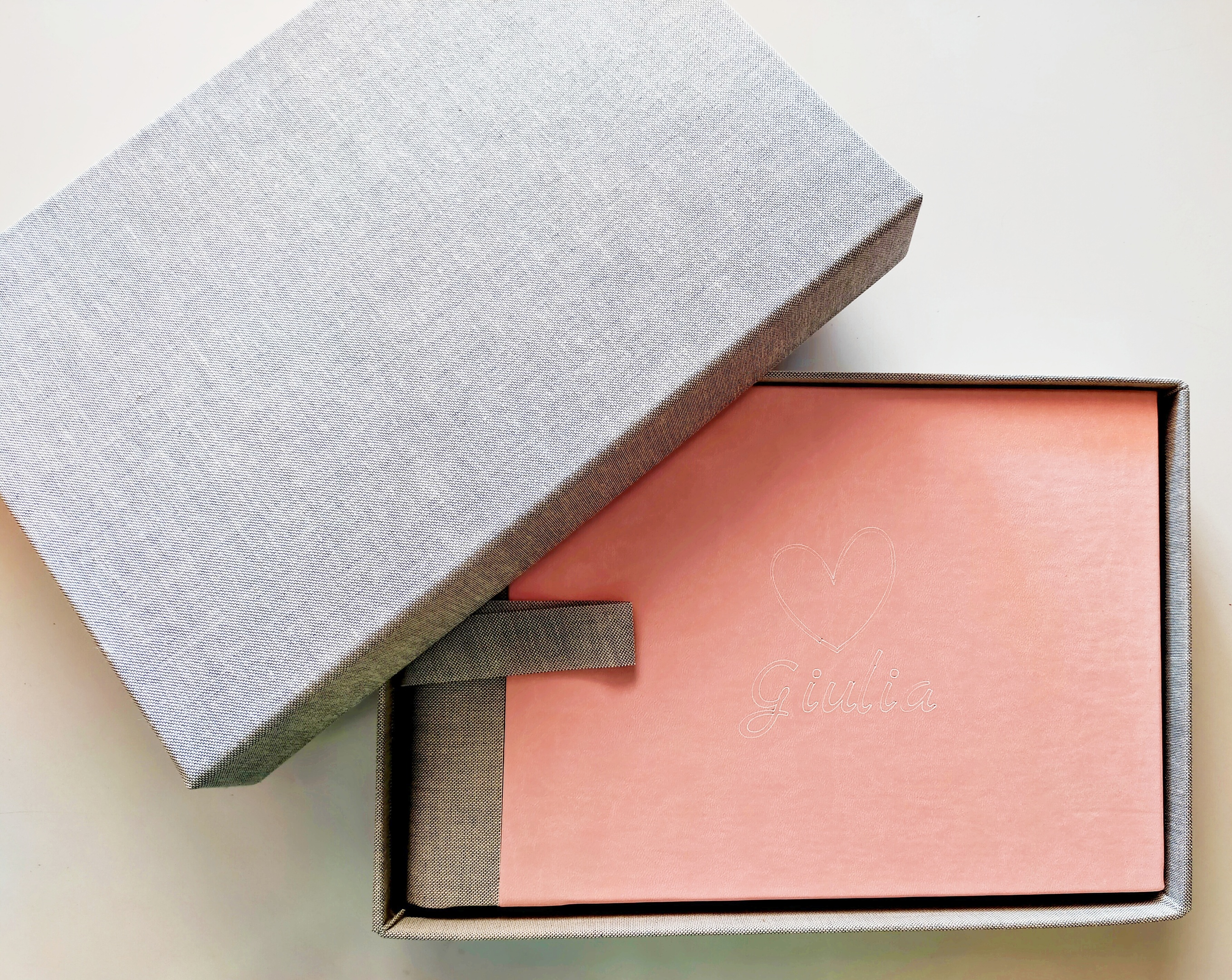 Album fotografico professionale Happy Color 30x20 cm, copertina rosa in ecopelle personalizzata con cuore e nome Giulia in bianco, dentro box di cartone rivestita in tessuto grigio con coperchio visibile, sfondo bianco - cofanetto fotografico professionale personalizzabile