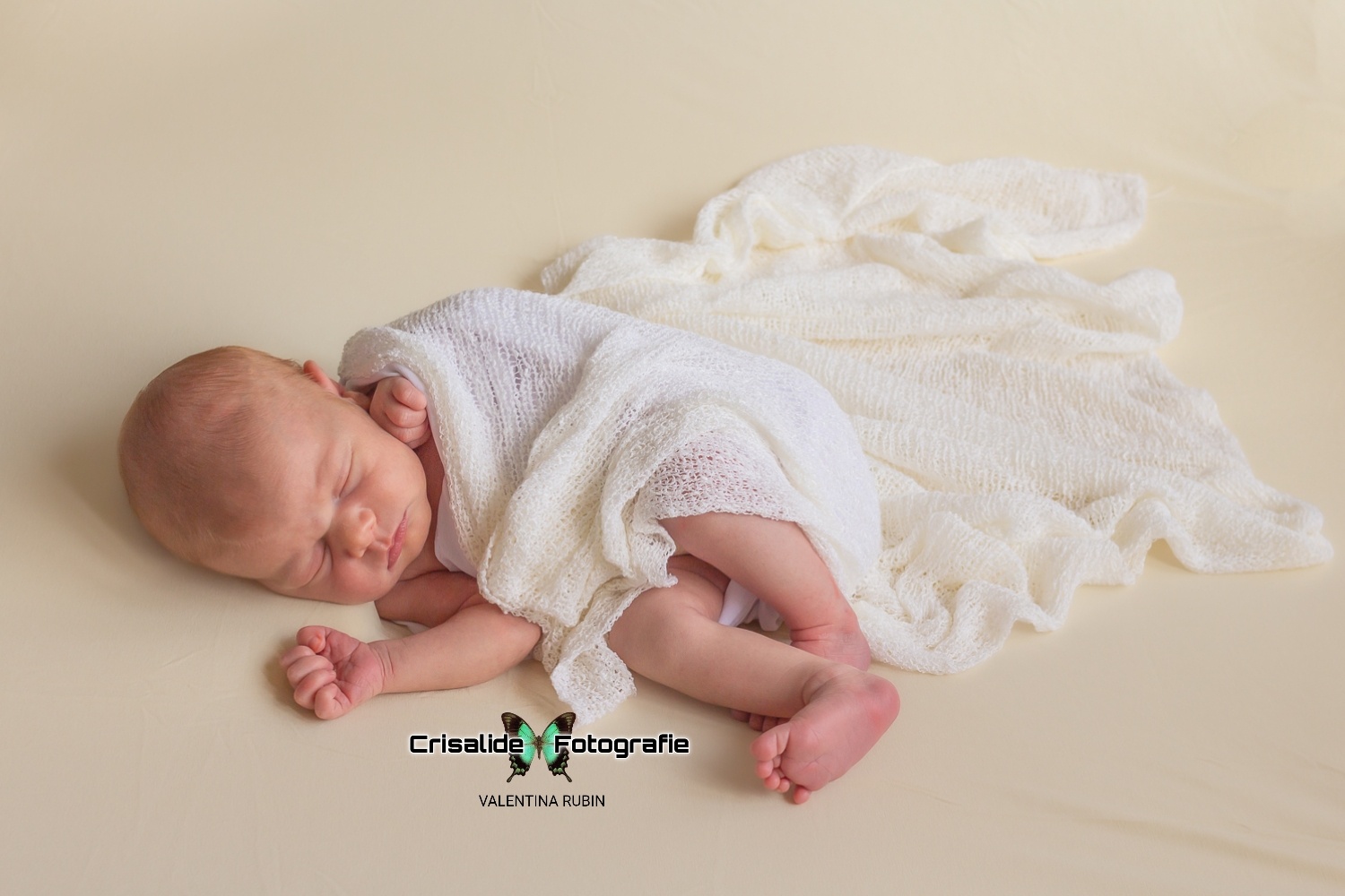Neonata che dorme di lato avvolta in uno scialle bianco ricamato su sfondo beige