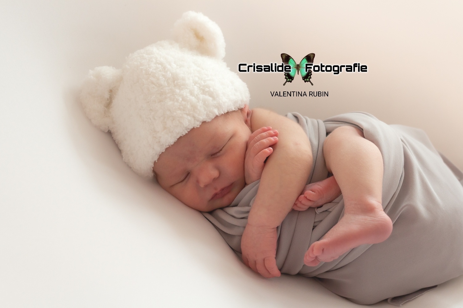 Neonato che dorme di lato, fasciato di grigio e berretto bianco con orecchiette