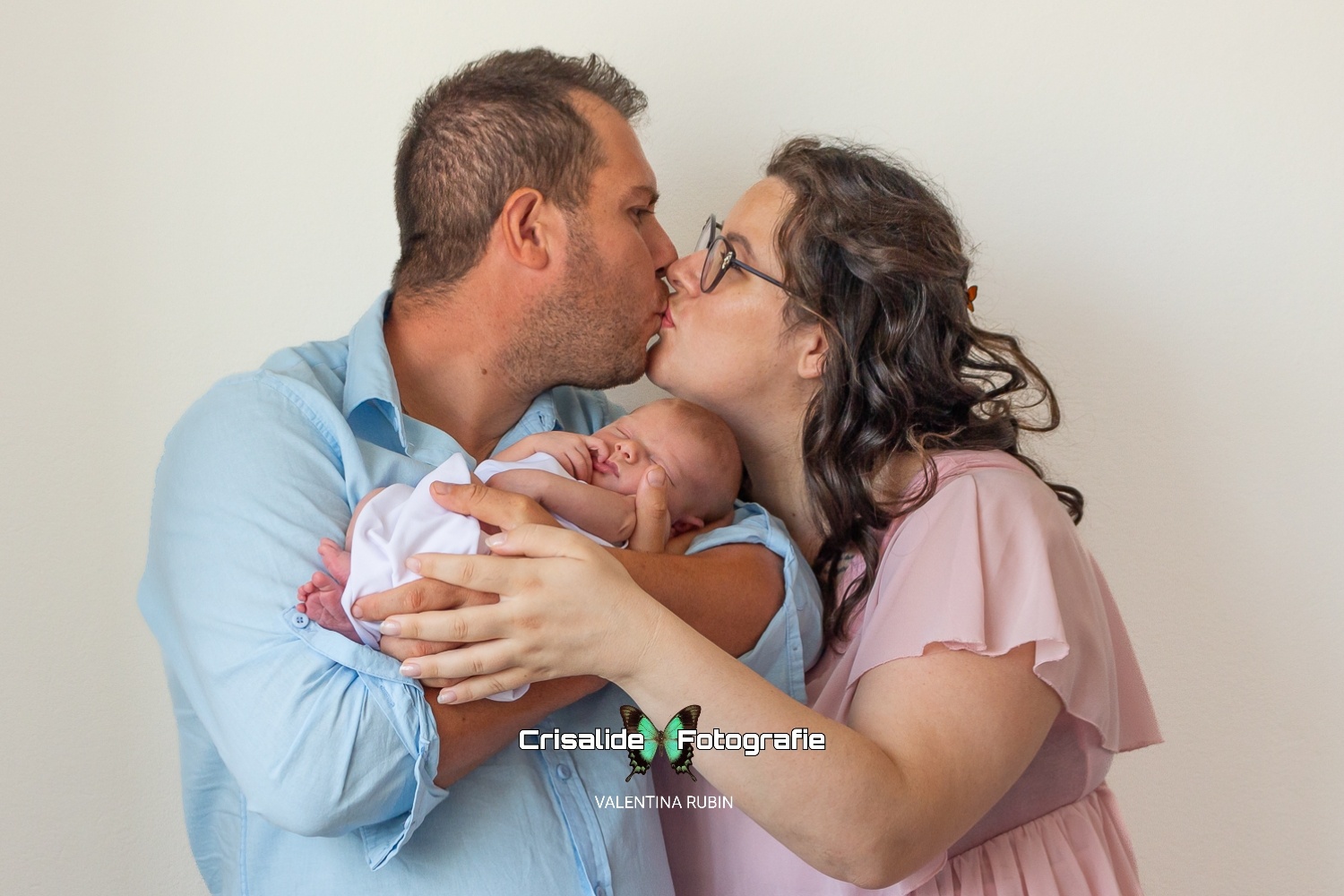 Mamma e papà che si baciano mentre tengono in braccio la neonata che dorme