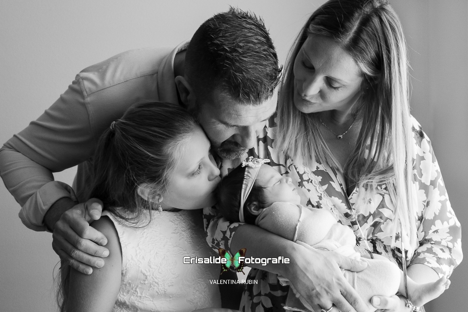 Mamma, papà e bambina insieme alla neonata che dorme, baci sulla testina, scatto newborn in bianco e nero