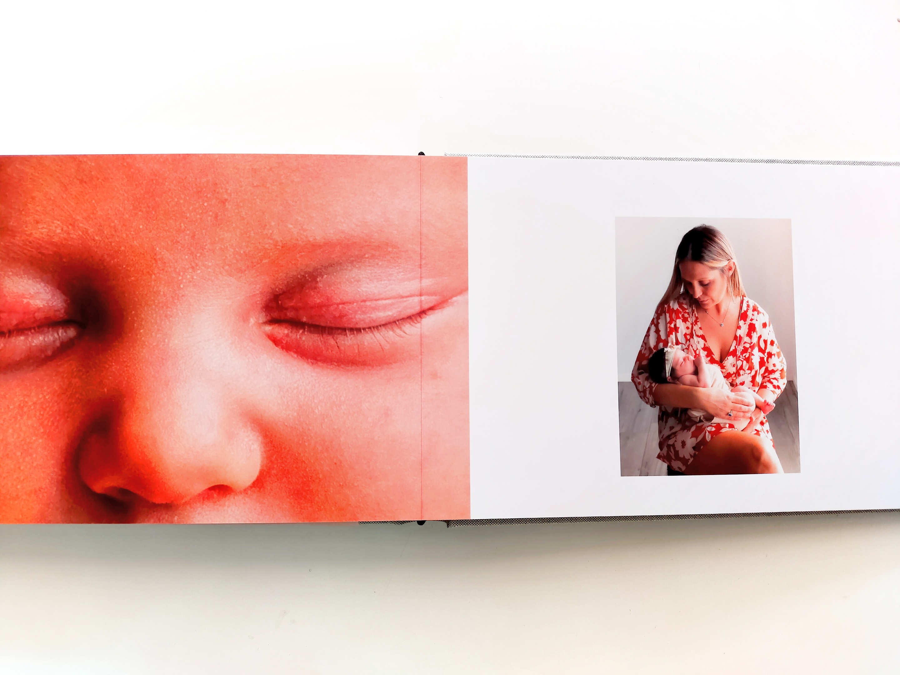 Album fotografico Happy Color aperto, pagina sinistra con dettaglio occhi della bambina, pagina destra con mamma seduta che tiene in braccio neonata, sfondo bianco - album professionale stampato con pagine rigide